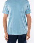 Man wearing light blue ocean beach t-shirt and navy day pants on white background