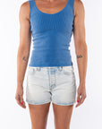 Woman wearing a blue ribbed tank top and light denim shorts on a white background