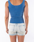 Back view of a woman wearing a blue ribbed tank with light denim shorts. 