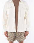 Man wearing a beige bucky shirt jacket, brown beach t-shirt and leopard camo printed day shorts on a white background