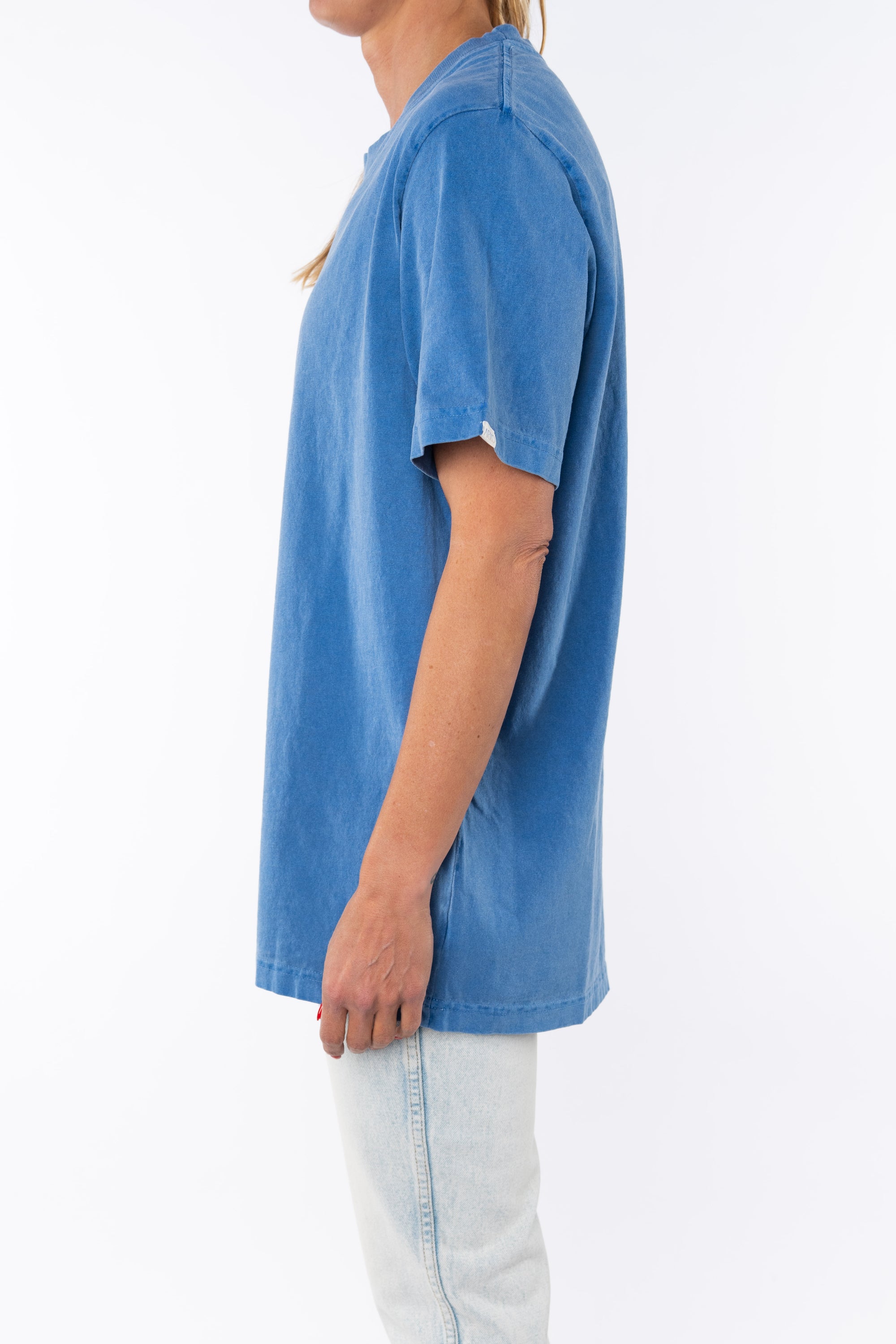Side view of a woman wearing a beach blue t-shirt with light denim jeans on a white background
