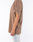 Woman wearing a brown beach t-shirt and light blue jeans on a white background