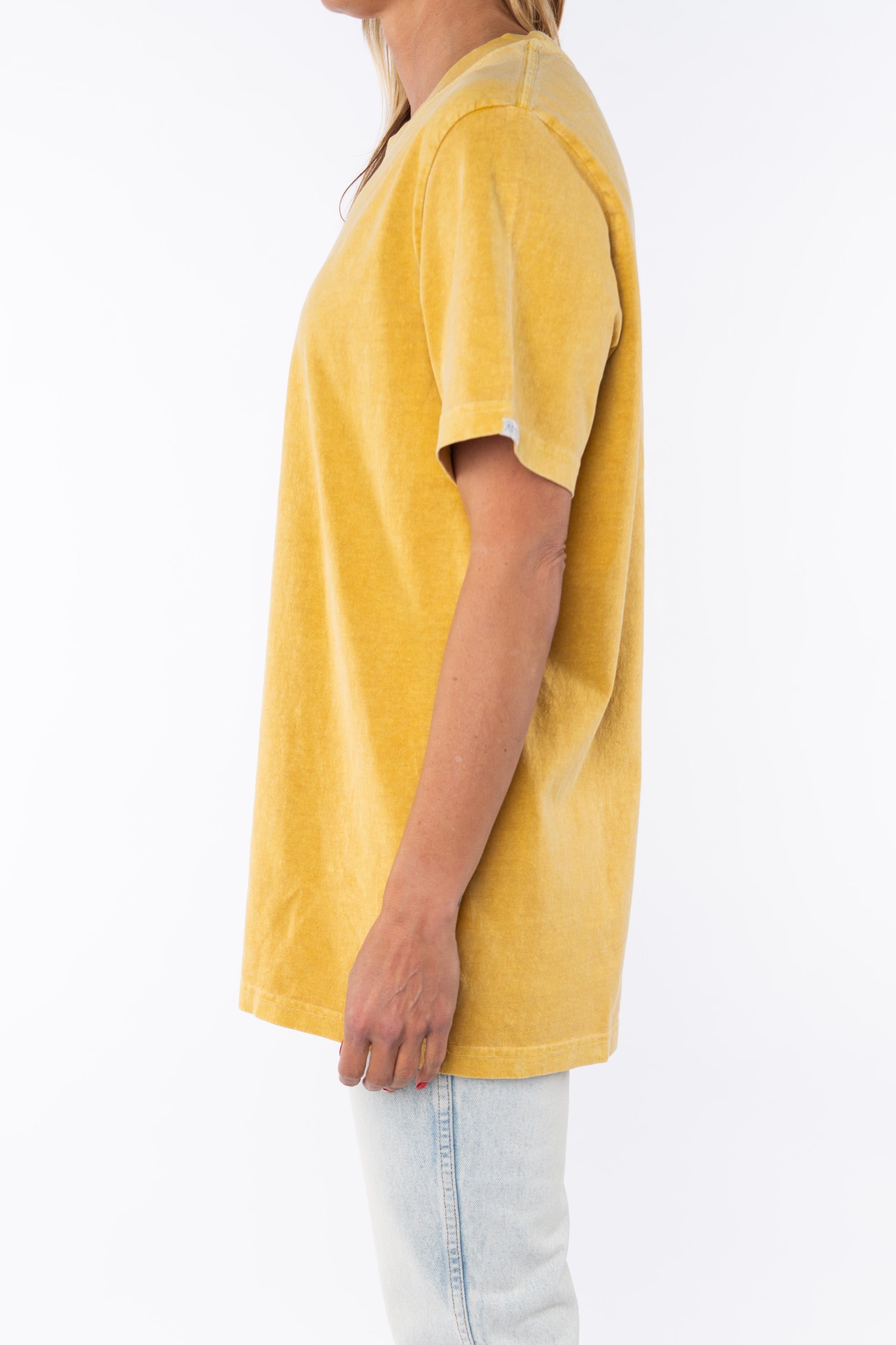 Side view of a woman wearing a sunrise yellow beach t-shirt and light denim jeans on a white background