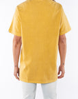 Back view of a woman wearing a sunrise yellow beach t-shirt and light denim jeans on a white background