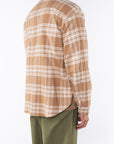 Side back view of a man wearing bucky beige plaid shirt jacket with army green day pants on a white background