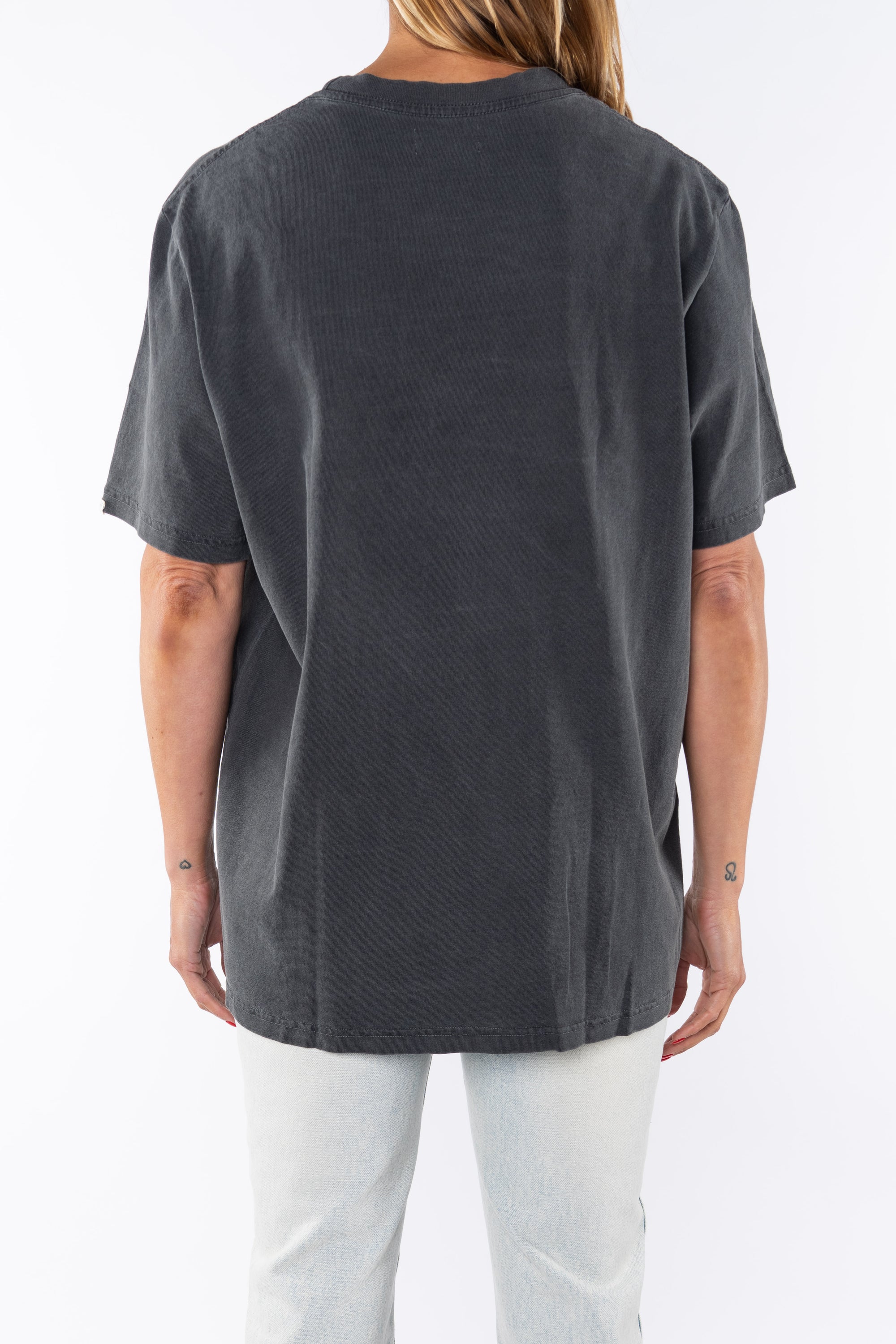 Back view of a woman wearing a dark gray beach t-shirt and light denim jeans on a white background