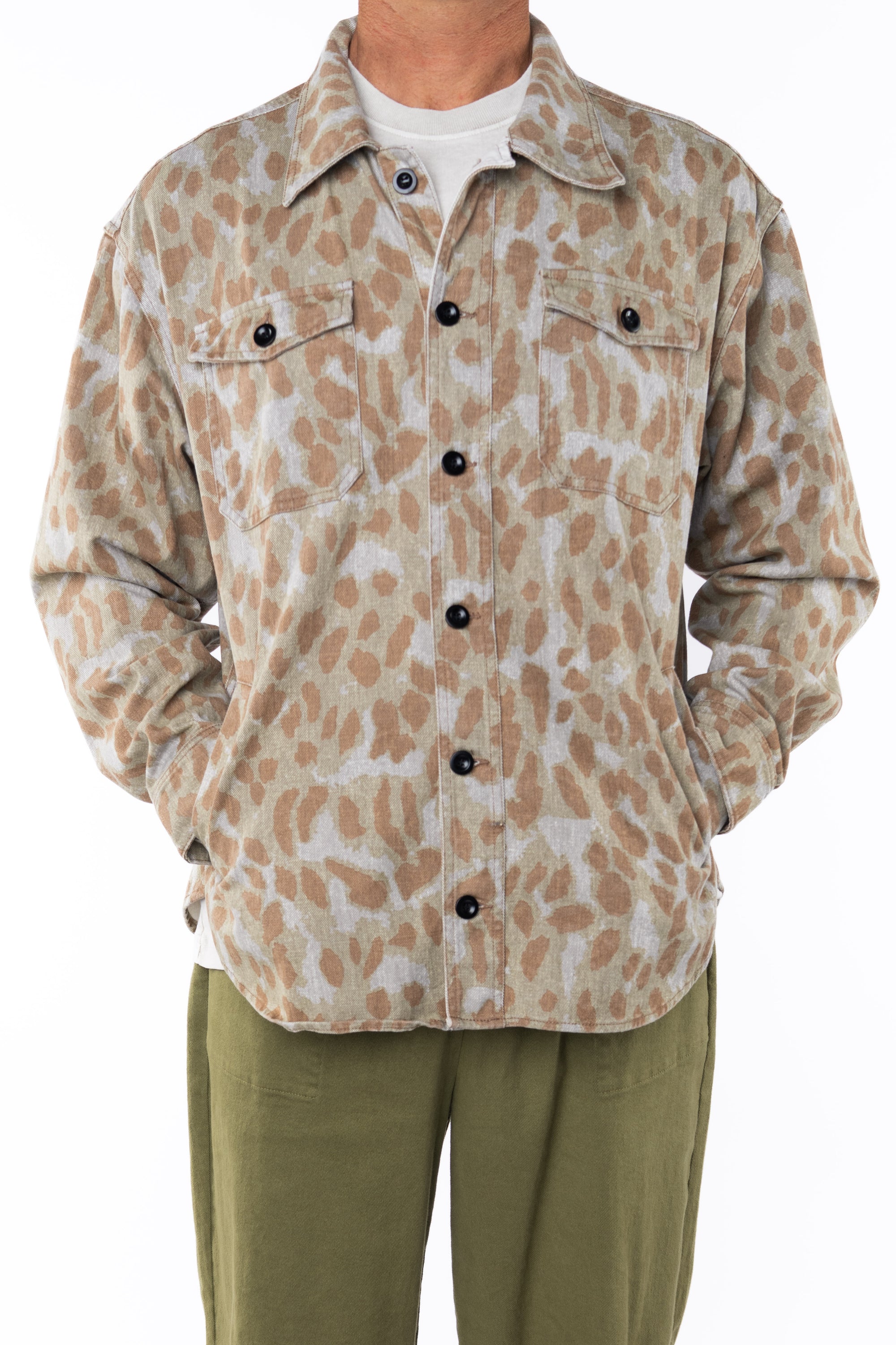 Person wearing a leopard camo bucky patterned jacket buttoned over a white shirt with army green day pants on a white background