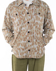 Person wearing a leopard camo bucky patterned jacket buttoned over a white shirt with army green day pants on a white background