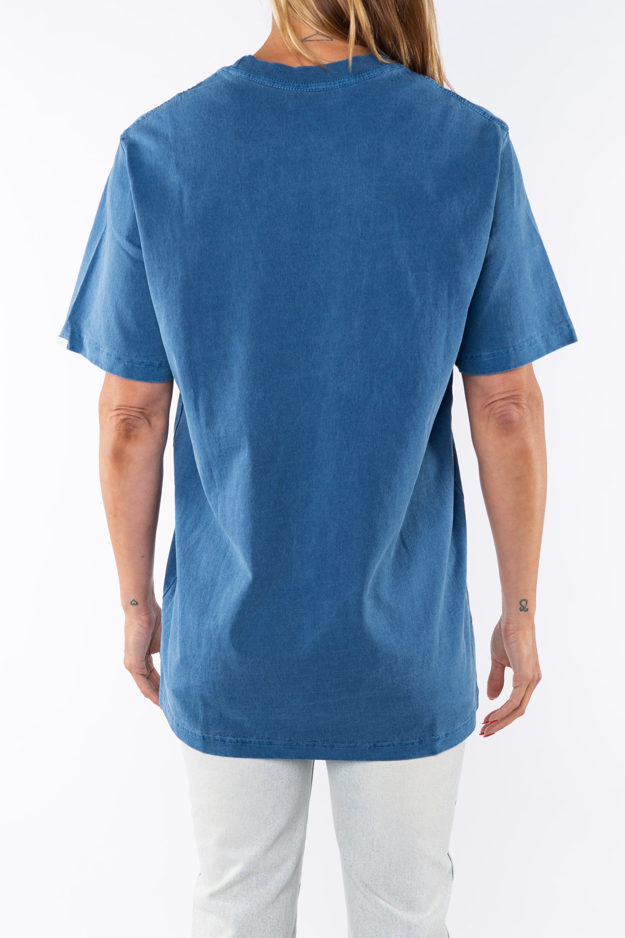 Back shot of a woman wearing Beach Crewneck T-shirt in Teal with Surf Jeans.