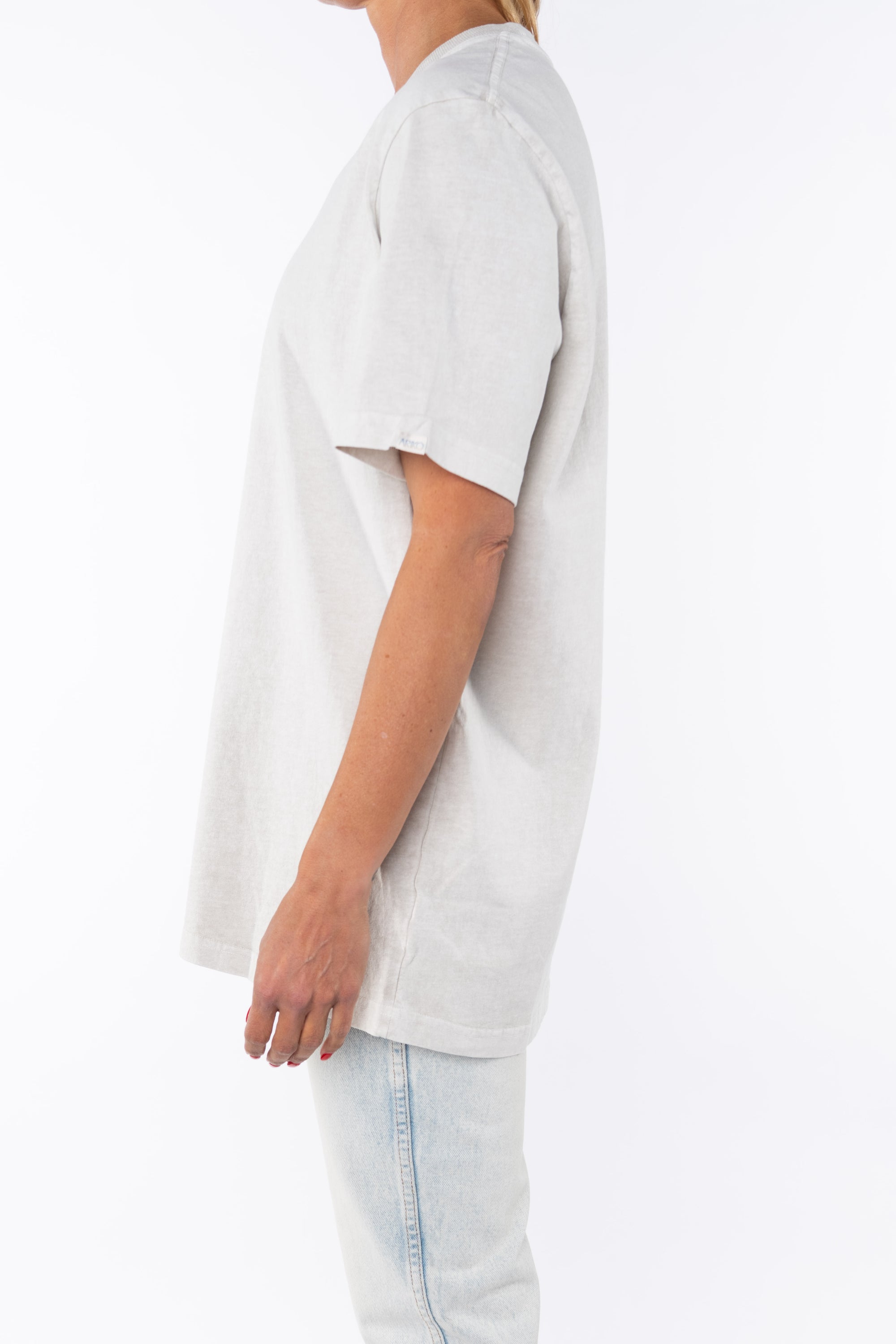 Side shot of a woman wearing woman wearing an oversized Crewneck T-shirt in cream with light washed denim jeans.