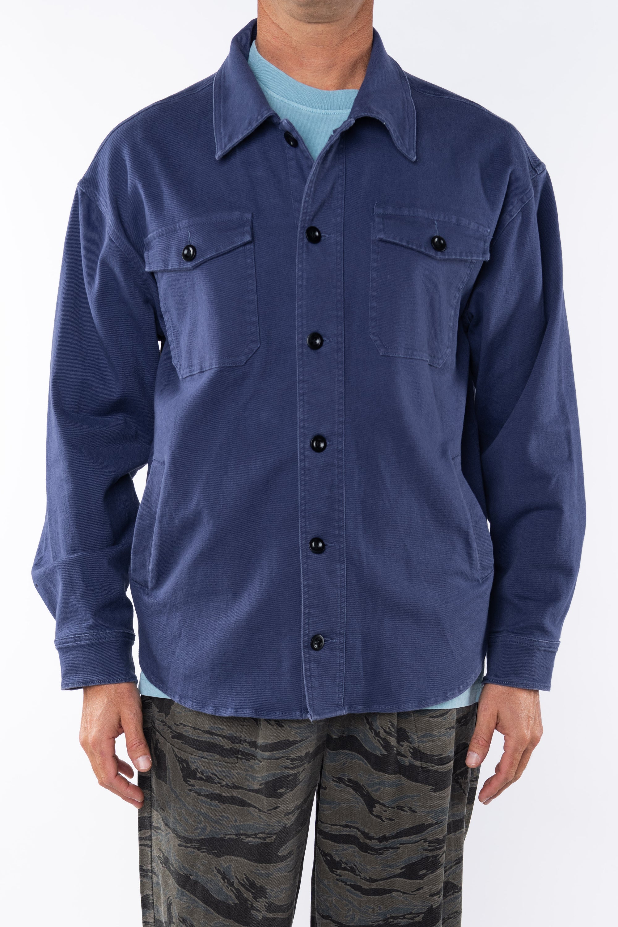 Man wearing the a shirt Jacket in navy with a Crewneck T-shirt in light blue and dark/blue and green Tiger Camo pants on a white background. 