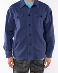 Man wearing the a shirt Jacket in navy with a Crewneck T-shirt in light blue and dark/blue and green Tiger Camo pants on a white background. 