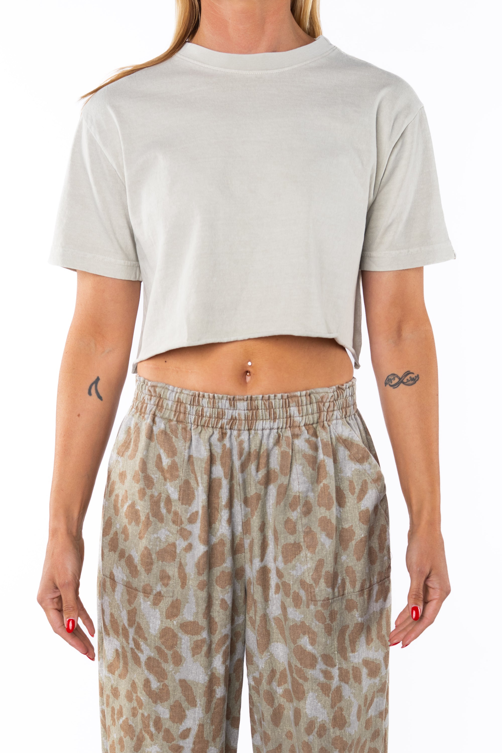 Woman wearing a cream cropped t-shirt and leopard patterned pants on a white background