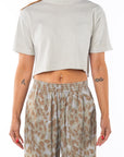 Woman wearing a cream cropped t-shirt and leopard patterned pants on a white background