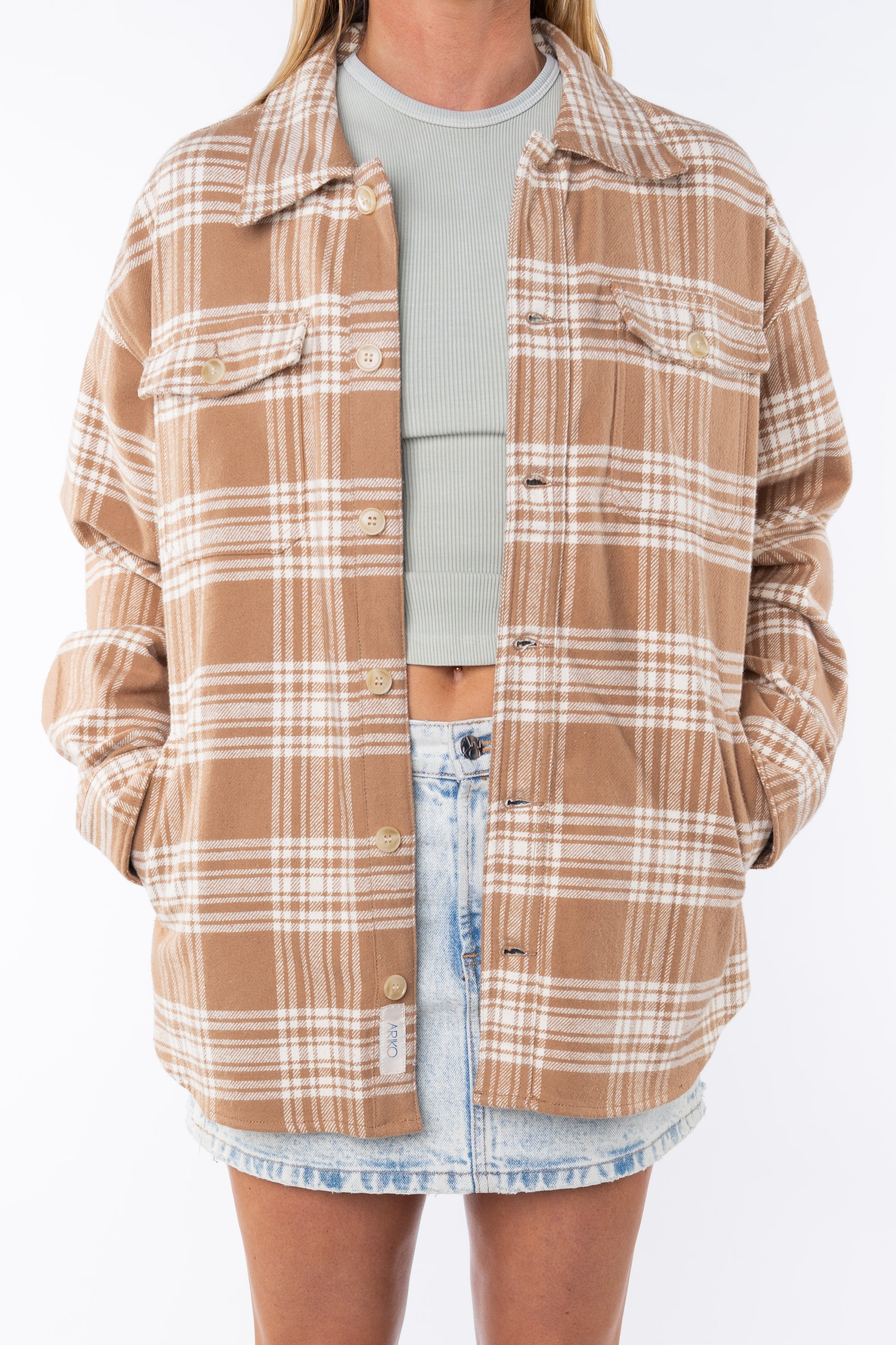 Woman wearing a flannel Split Hem Shirt Jacket in Beige/White Plaid with a crewneck Tank in cream and Denim mini Skirt on a white background. 