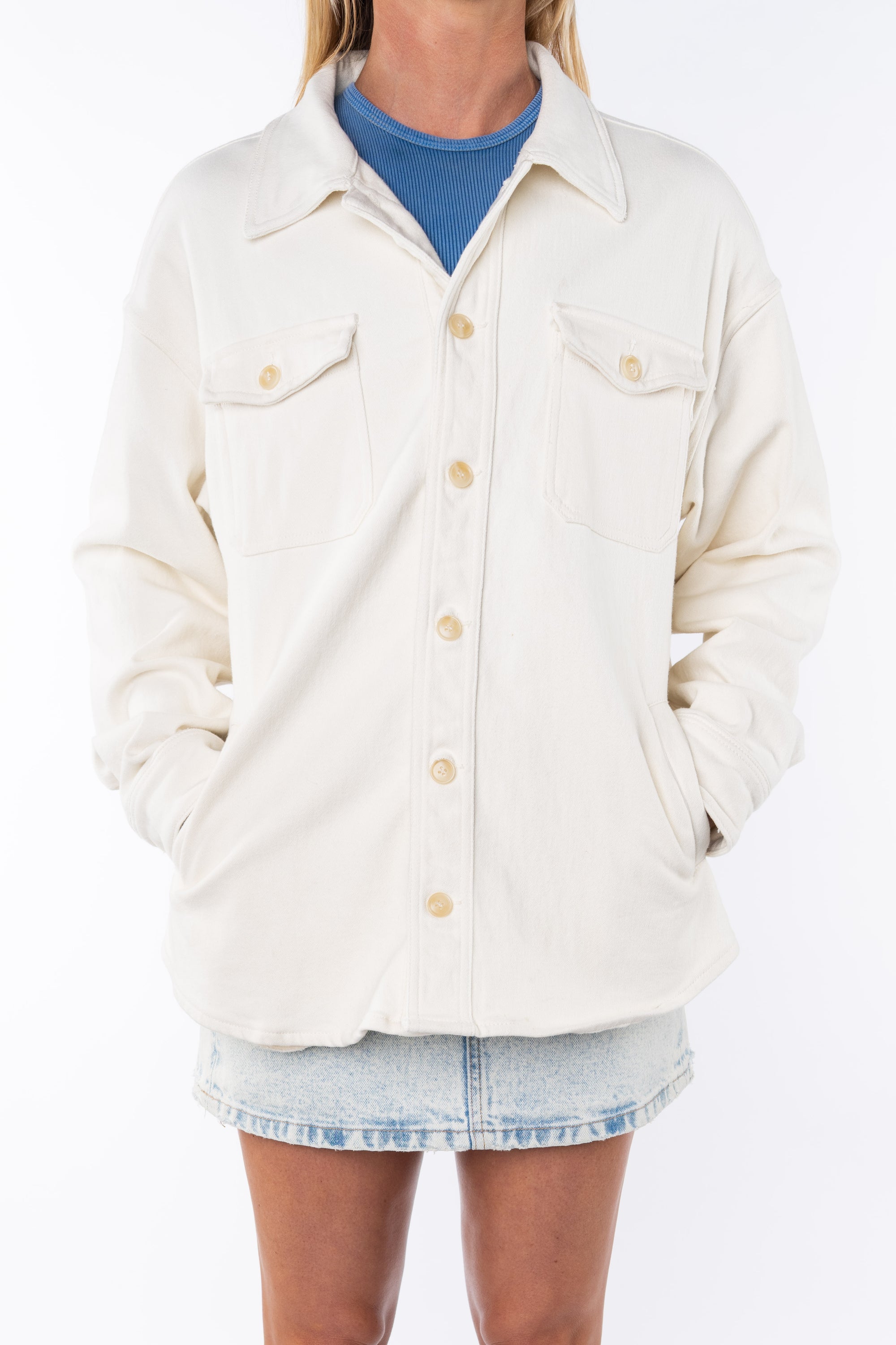 Woman wearing a Shirt Jacket in Beige with a crewneck tank in blue and a Denim mini Skirt on a white background. 