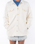 Woman wearing a Shirt Jacket in Beige with a crewneck tank in blue and a Denim mini Skirt on a white background. 