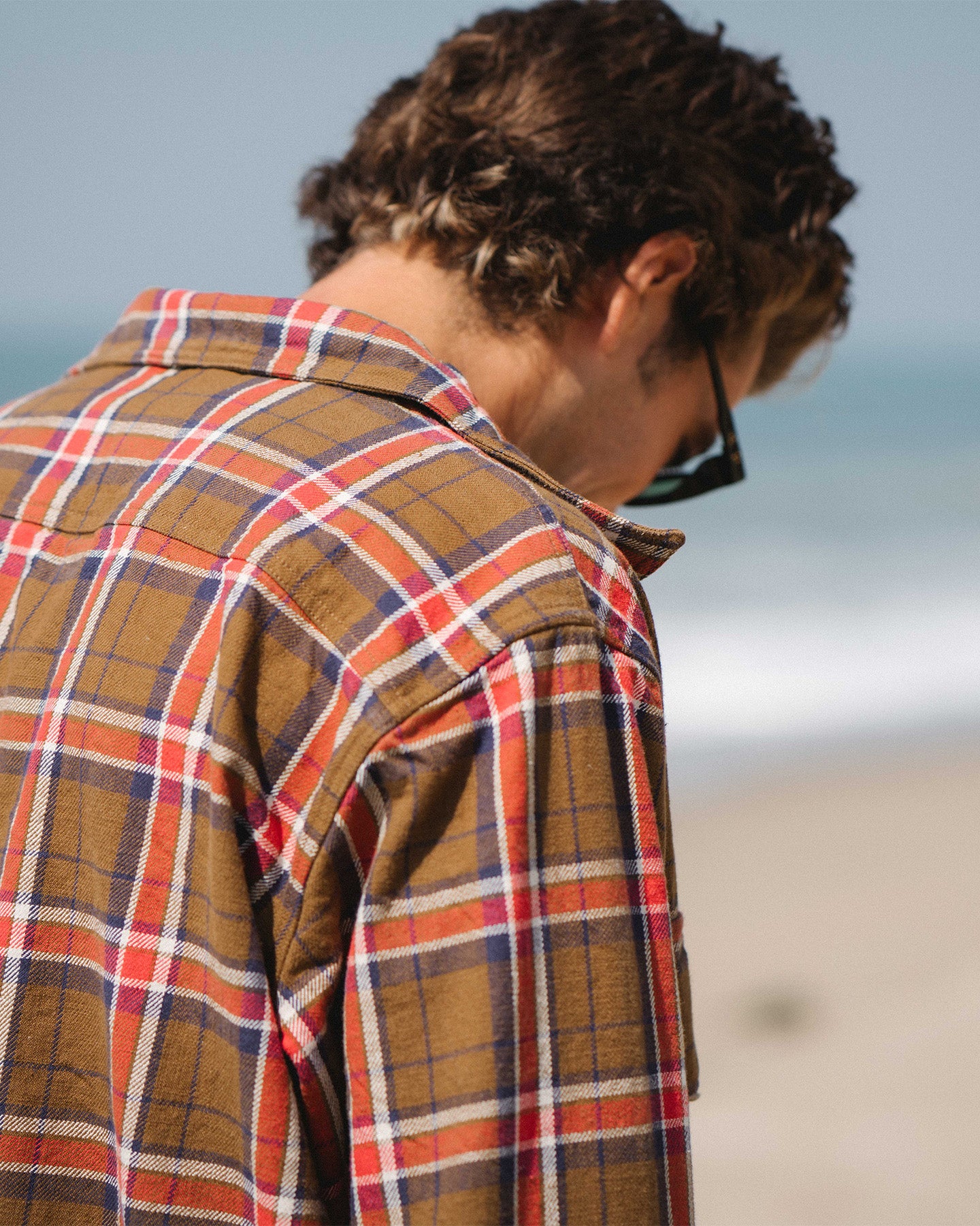 Man wearing a the brown/red bucky flannel on a beach. 