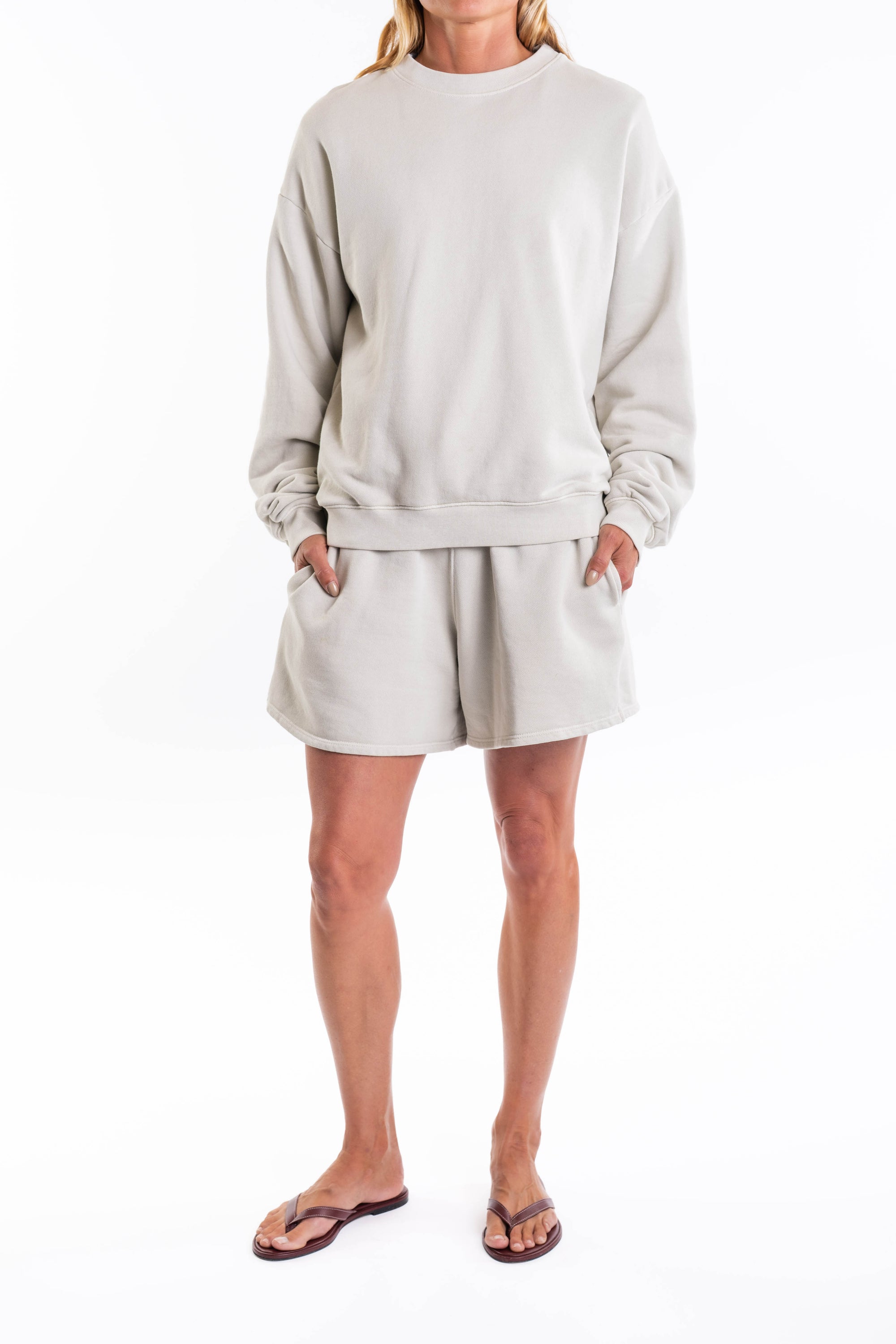 Woman wearing a light gray french terry sweatshirt and day shorts set on a white background