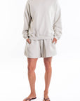 Woman wearing a light gray french terry sweatshirt and day shorts set on a white background