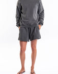 Woman wearing a dark gray french terry sweatshirt and day shorts set on a white background