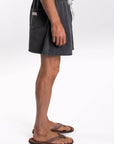 Side view of a person wearing dark gray shorts on a white background