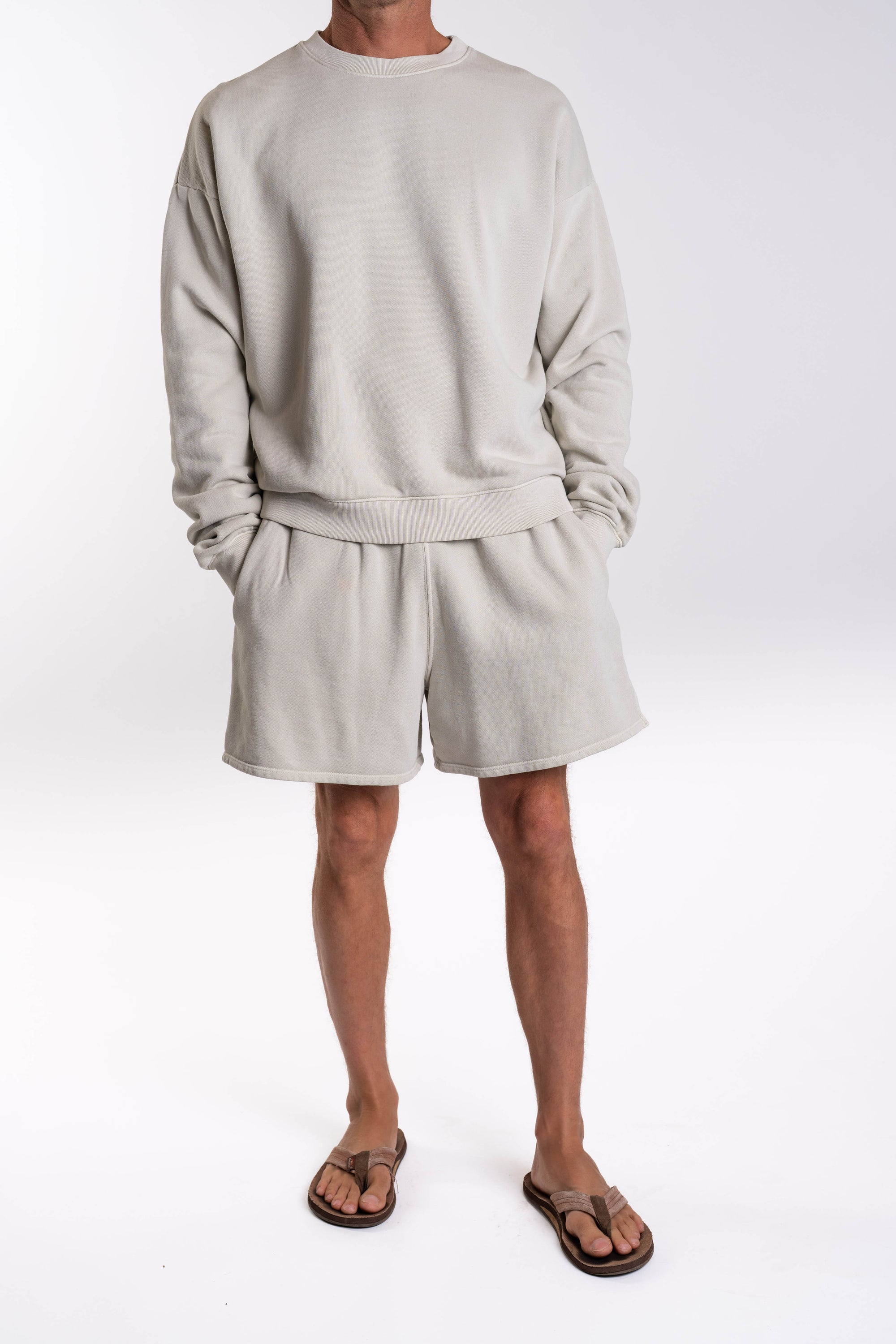 Person wearing a light gray french terry sweatshirt and day shorts set on a white background