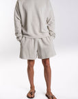 Person wearing a light gray french terry sweatshirt and day shorts set on a white background