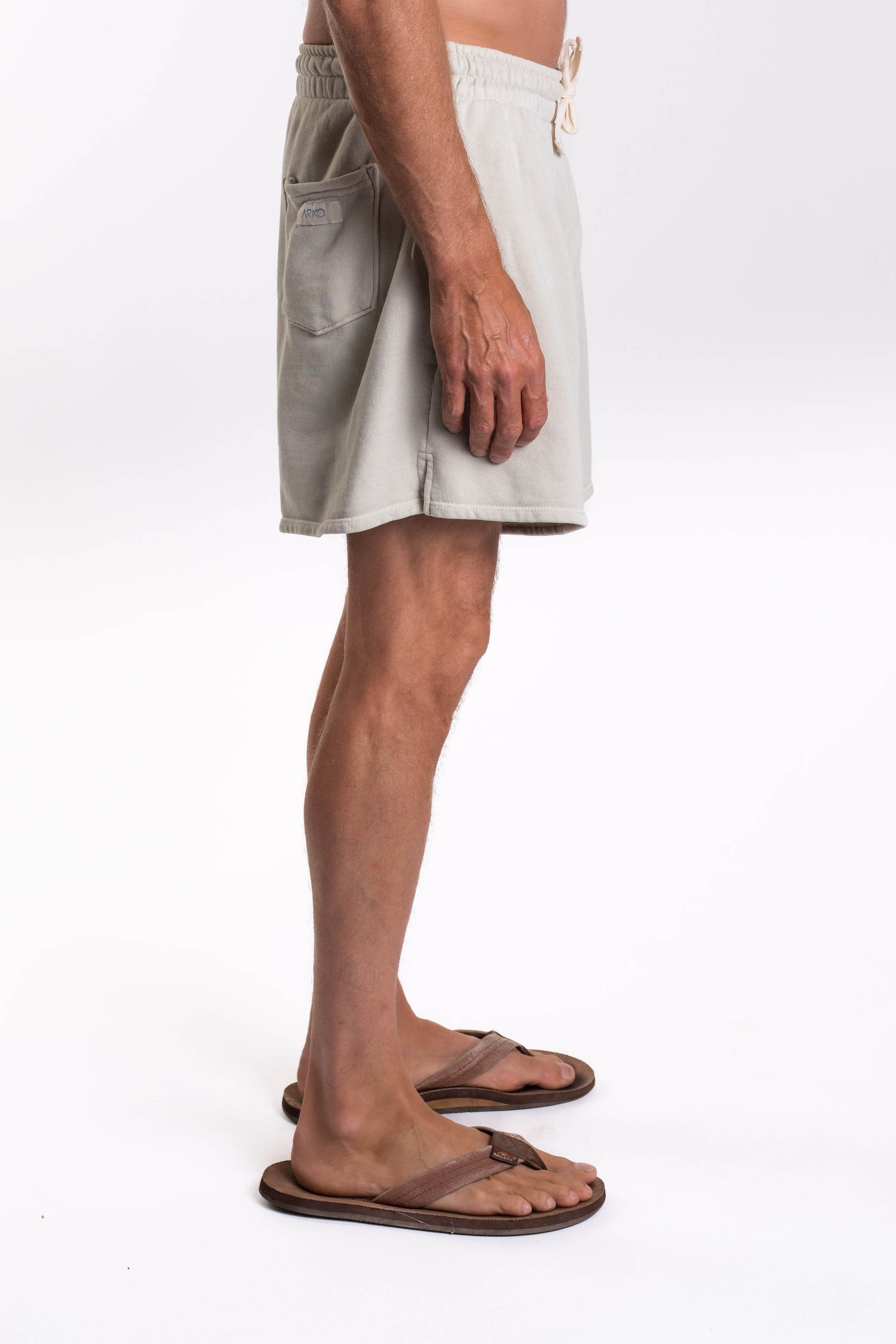 Side view of a person wearing light-colored shorts and sandals on a white background