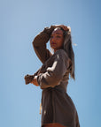 Woman in a brown french terry post surf crew sweatshirt and day shorts against a clear blue sky